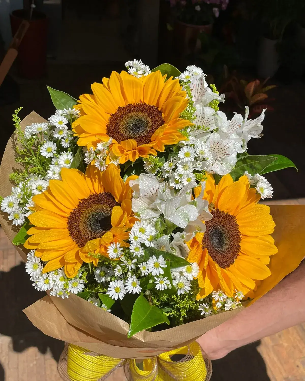 Buquê de girassóis e flores brancas embrulhado em papel kraft, da Flores Bellas